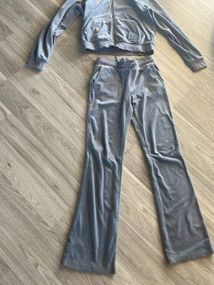 Blått velourset med ziptröja - Mysigt loungewear-set i mjuk blå velour. Setet består av en ziptröja med fickor och huva samt matchande byxor med dragsko i midjan och utsvängda ben. Perfekt för chill dagar hemma eller när du vill vara bekväm men ändå snygg. Storlek 168 på byxorna och 158-164 i koftan