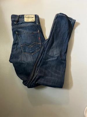 Mörkblå Replay Blue Jeans - Säljer ett par mörkblå Replay Blue Jeans med klassisk femficksdesign och kontrastsömmar. Jeansen har en patch med logga bak i midjan och snygga detaljer på bakfickan. Perfekta för en avslappnad och trendig stil.