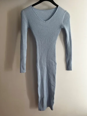 Ljusblå ribbad långärmad klänning - Säljer en ljusblå, ribbad klänning med lång ärm och v-ringning. Klänningen är kroppsnära och har en stretchig passform som framhäver siluetten. Perfekt för dig som gillar en enkel men stilren look. Säljes då jag tycker den blir för kort på mig som är 173 med långa med. Jag tycker om när den går ner hela vägen på bena men om man inte bryr sig om det passar den oss längre också! Använd ca 1 gång