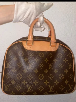 Louis Vuitton Monogram handväska - Vintage Louis Vuitton väska i klassisk och tidlös design med vacker patina som ger den ett äkta och exklusivt vintageuttryck.  Väskan säljs med authenticity card (obrandad kedja och körsbär-charm ingår som stylingdetalj).  Enligt medföljande autentiseringsintyg är väskan verifierad som 100% äkta Louis Vuitton, och det finns dessutom livstidsgaranti på autenticiteten kopplad till certifikatet, vilket bekräftar dess äkthet.  Skicket är mycket fint för sin ålder med normala spå