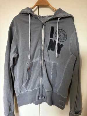 Grå my daily sweater hoddie - En grå mysig hoddie med lite sliten stil. Axelbredd är 45cm. Längden är 67cm.