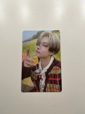 Enhypen Orange Blood photocard - Officiell photocard från Enhypens album Orange Blood. Kortet är rektangulärt och har ett färgstarkt motiv på framsidan med en person i rutigt vinrött och grönt plagg samt vit skjorta, och svart baksida med texten ORANGE BLOOD och ENHYPEN.