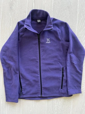 Lila fleecejacka från Haglöfs Junior - Lila fleecejacka från Haglöfs Junior med hel dragkedja framtill och två sidofickor med dragkedja. Mjuk och skön kvalitet, perfekt för lager-på-lager. Diskret Haglöfs-logga på bröstet och hög krage för extra värme. Rök- och djurfritt hem. Sparsamt använd.
