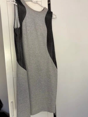 Grå ärmlös klänning med nätmönster - Snygg grå ärmlös klänning med svarta nätmönstrade paneler på sidorna som ger en sportig och modern look. Klänningen har dragkedja baktill .
