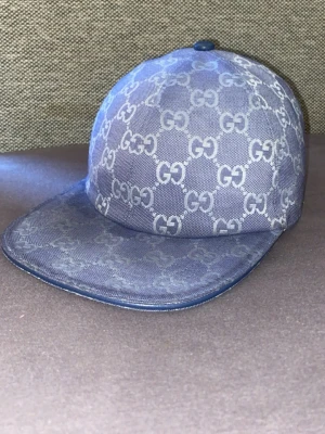 Blå keps från Gucci med GG-mönster - Säljer en blå keps från Gucci med det klassiska GG-monogrammet över hela kepsen. Kepsen har böjd skärm och är tillverkad i ett tåligt tygmaterial. Perfekt för dig som vill ha en stilren och lyxig accessoar till din outfit. Andvänd runt 2-3 veckor, bra skick. 700kr kan sänka vid seriösa köpare