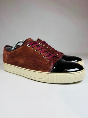 Lanvins - Snygga sneakers från Lanvin i vinrött mockaskinn med lockad svart tå. Strl 10 IT passar som 44 eu. Helt okej skick och inga skador eller så, hör av dig vid funderingar!