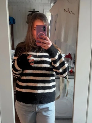 Svartvit randig stickad tröja - Stickad tröja med breda svarta och vita horisontella ränder. Tröjan har rund hals, långa ärmar och ribbstickade muddar vid ärmslut och nederkant. Perfekt för en avslappnad och trendig look.