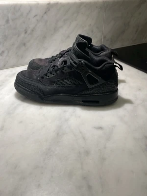 Svarta Air Jordan sneakers - Säljer ett par helsvarta Air Jordan sneakers med klassisk hög siluett. Skorna har meshpaneler på sidorna, robust snörning och detaljer i läder och syntet. Ikoniska Jumpman-loggan syns på plösen. Perfekta för dig som gillar streetwear och sportig stil.