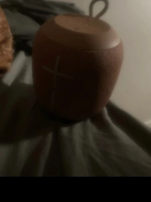 Ultimate Ears Wonderboom rosa högtalare - Säljer en portabel trådlös högtalare från Ultimate Ears i en snygg rosa färg. Högtalaren har rund form, grovt tygmaterial och tydliga volymknappar på sidan. Perfekt för att ta med sig tack vare den smidiga öglan upptill.