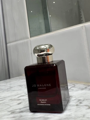 Jo Malone Scarlet Poppy Cologne Intense - En lyxig parfym från Jo Malone i doften Scarlet Poppy. Flaskan är mörkröd med en elegant silverfärgad kork och har en stilren, fyrkantig form. Innehåller 50 ml cologne intense som ger en unik och djup doftupplevelse.    Se sista bild hur mycket som finns kvar. 