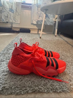 Röda Adidas TRAE YOUNG 2 - Snygga röda Adidas sneakers med stickad ovandel och tydliga svarta ränder på ovansidan. Skorna har en chunky sula och röda skosnören. Perfekt för dig som vill sticka ut med färg och sportig stil. Materialet är mesh och textil för skön komfort.