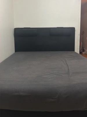  Signe är helt skön och helt  nytt  - Säljer en stilren svart säng med en mjuk, tygklädd gavel. Sängen har en enkel och modern design med två rektangulära kuddar på gaveln. Passar perfekt för dig som vill ha en minimalistisk look i sovrummet.