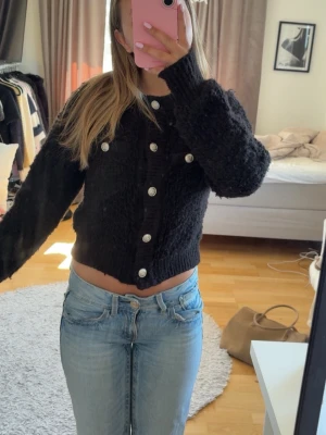 Svart kofta med knappar - Mysig svart kofta med knappar framtill. Koftan är stickad i ett fluffigt material.