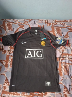 Manchester United Ronaldo tröja svart - Säljer en svart Manchester United matchtröja från Nike med röda detaljer, AIG-logga på bröstet och Premier League-märken på ärmarna. På ryggen står det Ronaldo och nummer 7 i vitt. Perfekt för fotbollsfans som vill sticka ut på planen eller läktaren.