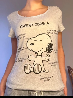 Grå Snoopy t-shirt med tryck - Säljer en ljusgrå t-shirt med stort Snoopy-tryck och texten 'A GOOD FRIEND' på framsidan. T-shirten har rund halsringning och korta ärmar. Perfekt för dig som gillar avslappnad och lekfull stil.