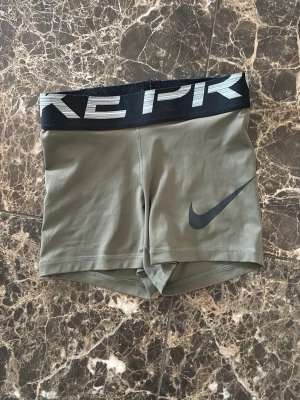 Gröna Nike PRO träningsshorts - Snygga gröna Nike Pro shorts med svart resår i midjan och stor Nike-logga på benet. Tight passform och korta ben, perfekta för träning eller gym. Tillverkade i stretchigt syntetmaterial för maximal rörelsefrihet. Använda en gång 