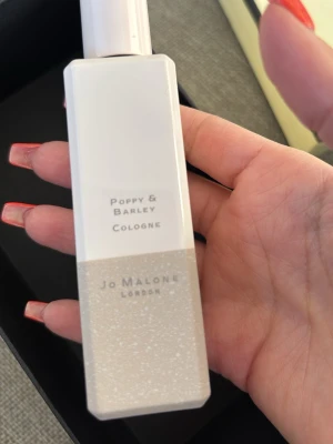 Jo Malone Poppy & Barley Cologne - Säljer en elegant parfym från Jo Malone, Poppy & Barley Cologne. Flaskan är rektangulär med vit och skimrande design, och har en stilren etikett. Perfekt för dig som gillar exklusiva dofter och snygg förpackning.