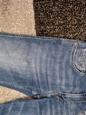 Replay jeans - Säljer ett par blå slim fit jeans med snygga slitningar och tvättade detaljer. Jeansen har klassisk femficksdesign och smala ben. Perfekta för en avslappnad och trendig look. Materialet är denim i bomull. W30