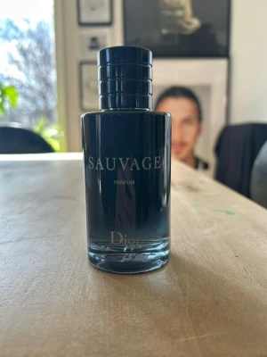 Dior Sauvage Parfum 100ml - Säljer en elegant parfymflaska från Dior, modellen Sauvage Parfum. Flaskan är mörkblå med svart lock och har en stilren, cylindrisk form. Texten på flaskan är i vitt och ger ett lyxigt intryck. Perfekt för dig som gillar exklusiva dofter.