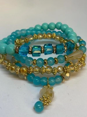 Turkost och guldigt pärlarmband - Flera armband i turkosa och guldiga toner med olika former av pärlor, inklusive runda och fyrkantiga. Armbanden har detaljer i guld och ett hängsmycke med pärlor. Ej använd utan kommer från min small business. 