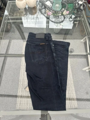 Nudie Jeans Skinny Lin W30/L32 - Säljer mina Nudie Skinny Lin i W30/L32. Riktigt snygg mörk svart/blå wash med clean fit som sitter fett bra.  98% organic cotton och 2% elastane så de har lite stretch och är sköna på. Bra skick och passar perfekt till både sneakers och hoodie eller mer clean outfit.  Sjukt bra vardagsjeans som funkar till allt, säljs bara för att de inte används längre.