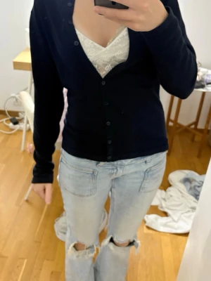 Mörkblå basic kofta med knappar - En enkel och stilren mörkblå kofta med långa ärmar och knäppning framtill. Koftan har en smal passform och är perfekt att bära över ett linne eller t-shirt. Materialet känns mjukt och stretchigt, vilket gör den bekväm för vardagsbruk.