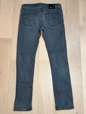 Mörkgrå Jacob Cohen Jeans - Snygga mörkgrå jeans från Jacob Cohen med femficksdesign och svarta sömmar. Jeansen är 106 cm lång och är i storlek W34.