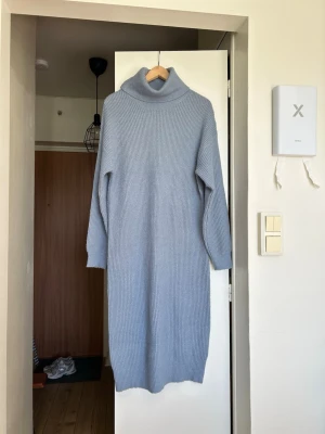 Ljusblå stickad poloklänning - Mysig ljusblå stickad klänning med polokrage och lång ärm. Klänningen har en rak passform och ribbad struktur, perfekt för kyligare dagar. Enkel och stilren design som är lätt att matcha med olika accessoarer.