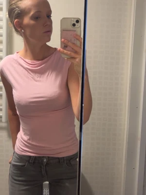 Ljusrosa ärmlös topp - Säljer en ljusrosa, ärmlös topp med rund halsringning. Toppen har en slim passform och är tillverkad i mjukt bomullsmaterial. Perfekt att matcha med jeans eller kjol för en enkel och stilren look.