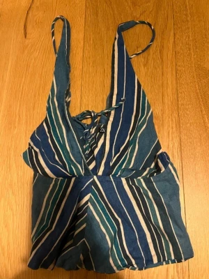 Randig linnetopp från Zara - Säljer en snygg randig linnetopp från Zara i blå, vit och grön. Toppen har djup v-ringning, smala axelband och knyt i ryggen. Perfekt för sommaren och ger en chill vibe till din outfit.