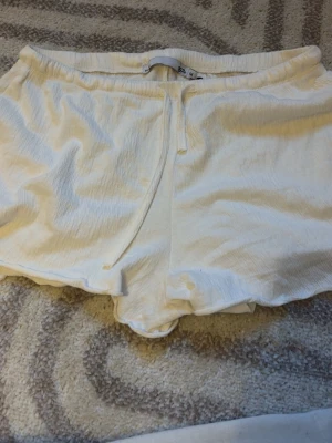 Vita shorts med snörning från lager 157 - Säljer ett par vita shorts från lager 157 i storlek M. De har en mjuk, lite skrynklig struktur och snörning i midjan för skön passform. Perfekta för varma dagar och enkla att matcha med olika toppar. Har aldrig använts så är gott som nya.