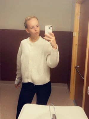 Vit fluffig kofta med knappar - Mysig vit kofta med rund hals och stora knappar framtill. Koftan har en fluffig, mjuk textur och långa ärmar. Perfekt för lager på lager och enkel att matcha med olika outfits.