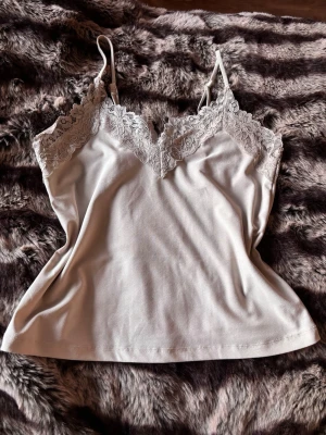 Krämvit spets linne  - Supersöt krämvit spetslinne med tunna axelband och vacker spets längs v-ringningen. Perfekt att styla lager på lager eller bära som den är. Mjuk och skön känsla, lätt att matcha till olika looks. Smink streck på de men inget man ser när man bär de 