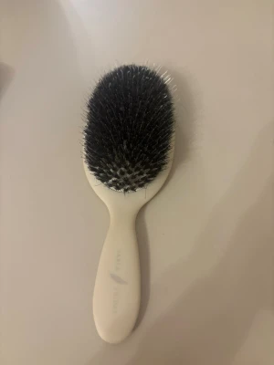 Vit hårborste från Sable & Sable - Säljer en stilren hårborste från Sable & Sable med vitt handtag och svarta borst. Handtaget är ergonomiskt format för ett bra grepp och borsten har täta, mjuka strån som passar perfekt för att reda ut håret utan att slita. Perfekt accessoar till din hårvårdsrutin.