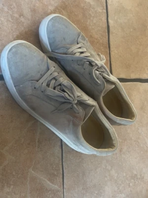 Vagabond skor med vit sula - Snygga beige sneakers i mocka med klassisk låg profil och vita sulor. Skorna har matchande beige skosnören och en stilren design utan synliga loggor. Perfekta för dig som gillar en clean och enkel look.