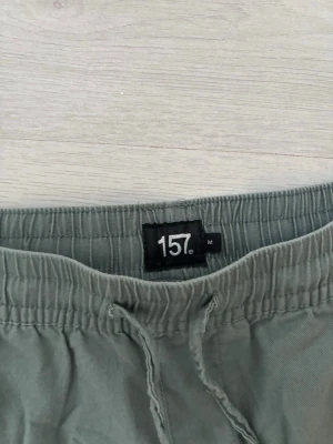 Gröna shorts med snörning från 157 - Säljer ett par gröna shorts från 157 i storlek M. De har elastisk midja med snörning och två sidofickor. Perfekta för sommaren och riktigt sköna att bära till vardags. Materialet känns som bomull och shortsen har en avslappnad passform.