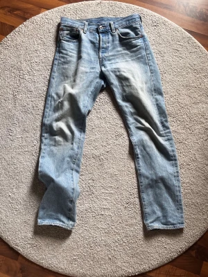 Levi's ljusblå raka jeans - Säljer ett par klassiska ljusblå jeans från Levi's med raka ben och fem fickor. Jeansen har en snygg tvättad look och läderpatch bak i midjan. Perfekta för en avslappnad och trendig stil. Materialet är 100% bomull.