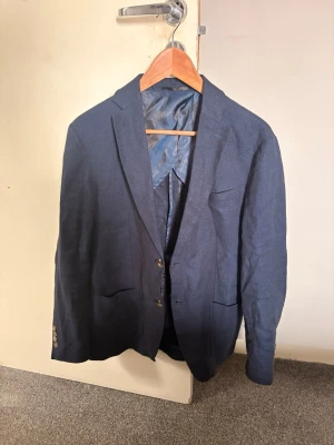 Mörkblå linne kavaj set från John Henric - Stilren mörkblå linne kavaj set från John Henric med två knappar framtill och klassisk passform. Kavajen har slät yta, diskreta fickor och helfodrad insida i matchande blått tyg. Perfekt för en dressad look.