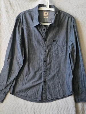 Randig skjorta från Lee i bomull - Snygg mörkblå skjorta från Lee med tunna vita ränder och klassisk krage. Skjortan har lång ärm, bröstficka och knappar framtill. Slim fit-modell i mjuk bomull som passar perfekt till jeans eller chinos.