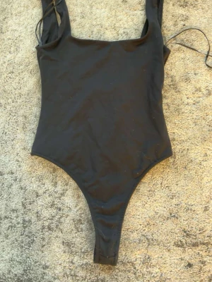 Svart klassisk baddräkt - En stilren svart baddräkt med raka axelband och högt skuren benlinje. Baddräkten har en enkel, klassisk design med djup rygg och är tillverkad i stretchigt material som passar perfekt för stranden eller poolen.