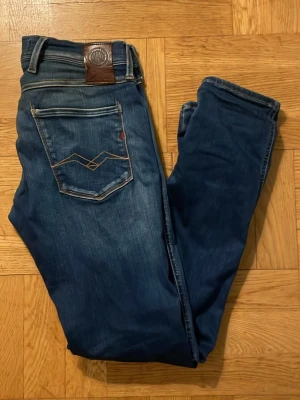 Replay Jeans - Säljer ett par blå jeans från Relax med snygga slitningar framtill och kontrastsömmar. Jeansen har klassisk femficksmodell, läderpatch bak i midjan och coolt broderi på bakfickan. Materialet är denim i bomull med en något smal passform. Skriv om du har frågor!
