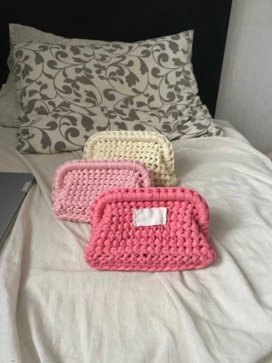 Handgjorda virkade necessärer - Tre handgjorda virkade necessärer i olika färger: rosa, ljusrosa och beige. De har en rektangulär form och är tillverkade i tjockt garn. Perfekta för småprylar eller smink.  säljs styckvis .