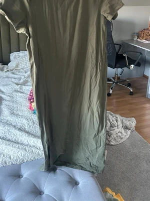 Olivgrön t-shirtklänning i bomull - Enkel och stilren olivgrön t-shirtklänning i mjuk bomull. Klänningen har korta ärmar och rak passform, snygg med ett bälte i mitten. Storlek xs