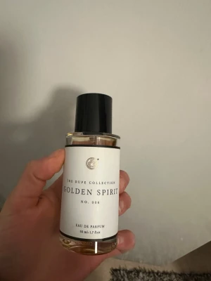 Golden Spirit Eau de Parfum 50ml - Golden Spirit No. 006 från The Dupe Collection är en Eau de Parfum i en stilren, rund glasflaska med svart plastlock. Parfymen har en gyllene vätska och minimalistisk vit etikett. Flaskan rymmer 50 ml och passar perfekt för dig som gillar eleganta dofter.