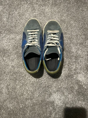 Blå och grå Phillippe Models - Snygga sneakers i blått och grått med mockadetaljer och vita skosnören. Skorna har lågt skaft och en kontrasterande grön häl. Perfekta för dig som gillar en avslappnad och stilren look.