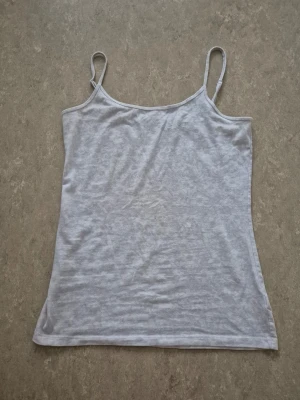 Linnetopp - Säljer en ljusgrå linnetopp med tunna axelband och rak passform. Toppen är ärmlös och har en clean, minimalistisk look som passar perfekt till sommaren. Materialet känns mjukt och lätt mot huden.