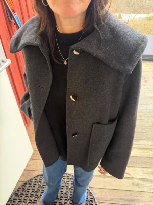 Mörkgrå ullrock med krage - Snygg mörkgrå ullrock med oversized krage och stora framfickor. Så perfekt nu till våren. I väldigt bra skick!!