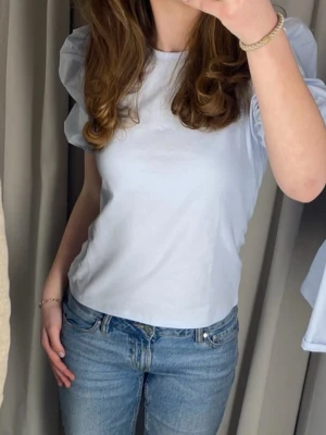 Ljus blå topp med puffärm - Snygg ljus blå topp med puffiga kortärmar och rund halsringning. Enkel och stilren design som passar till mycket. Tillverkad i mjukt material för en bekväm känsla. Perfekt nu inför våren!🩷