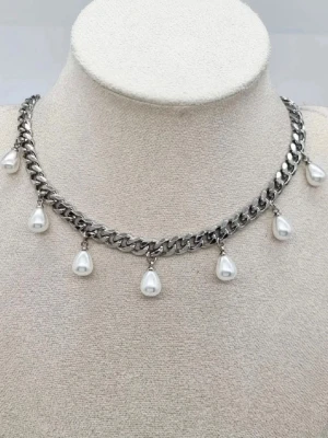 Chunky silverhalsband med pärldroppar - Stilrent halsband i silverfärgad metall med kraftig kedja och hängande droppformade vita pärlor. Kedjan har justerbar längd och pärlorna ger en cool kontrast till den chunky designen. Perfekt för att lyfta din outfit med en trendig touch.