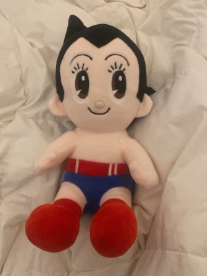 Astro Boy mjukisdjur från Tezuka - Säljer ett gulligt Astro Boy mjukisdjur från Tezuka Productions. Dockan har svart hår, stora bruna ögon, blå shorts med rödvit detalj och röda skor. Perfekt för samlare eller som present till animefans!